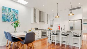 Une cuisine moderne avec des meubles blancs, un îlot central doté de tabourets, et un coin repas avec une table et des chaises.