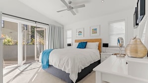 Une chambre avec un lit, un ventilateur de plafond, un bureau et une vue sur l’extérieur.