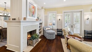 A living room with a fireplace, comfortable seating, and a view through French doors. - Short Walk to Beach Club, Close to Seaside | 3BR Home + Carriage House (Santa Rosa Beach)