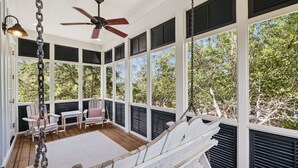 A covered porch with white railings, a ceiling fan, and a swing chair. - Short Walk to Beach Club, Close to Seaside | 3BR Home + Carriage House (Santa Rosa Beach)