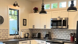 Una cocina moderna con armarios blancos, un microondas de acero inoxidable, horno empotrado y una isla grande con sillas de mimbre.