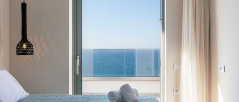 A hotel room with a bed, a hanging light fixture, a view of the sea through a window, and a curtain.