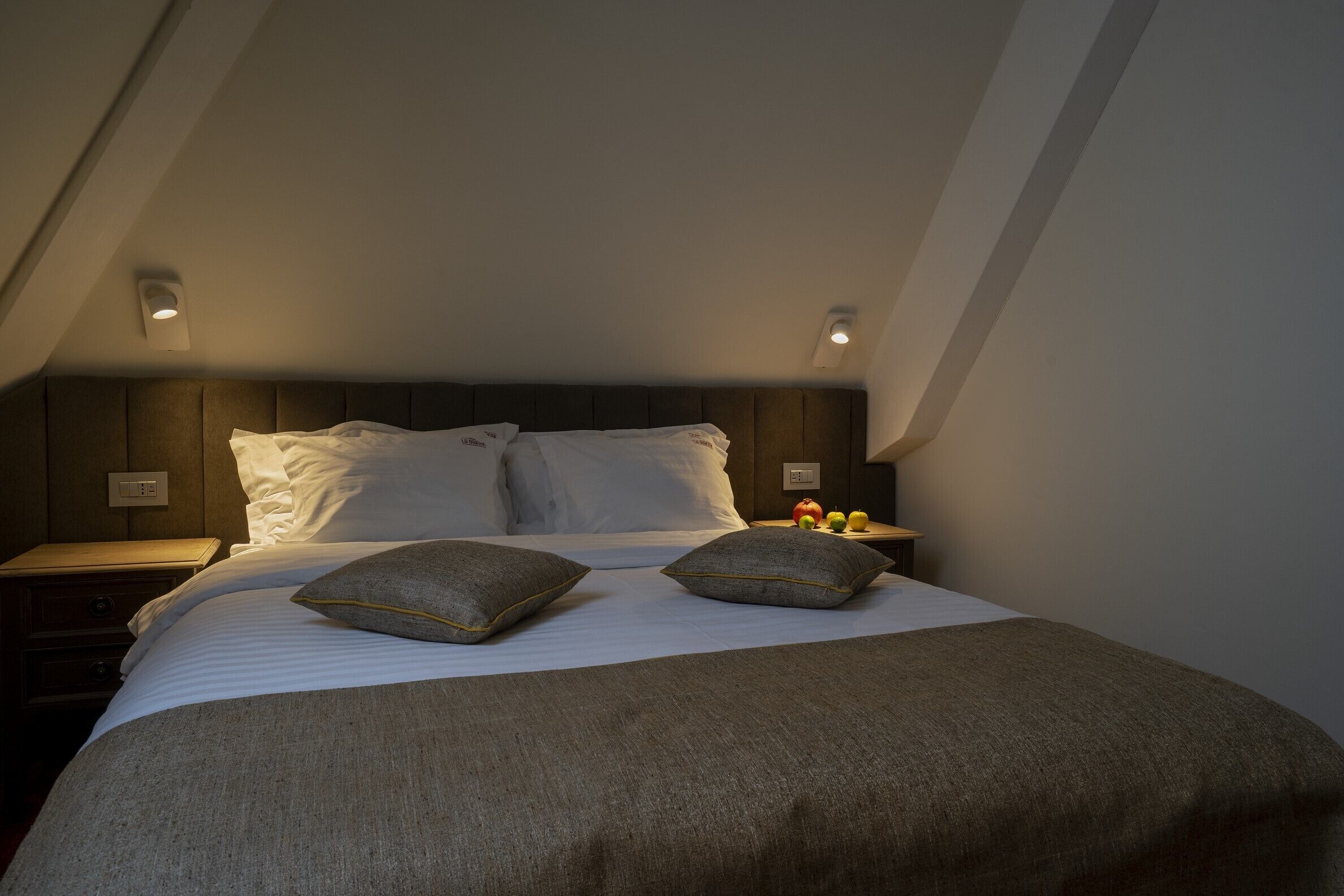 A bedroom with a bed, pillows, a nightstand, and a wall-mounted light fixture.