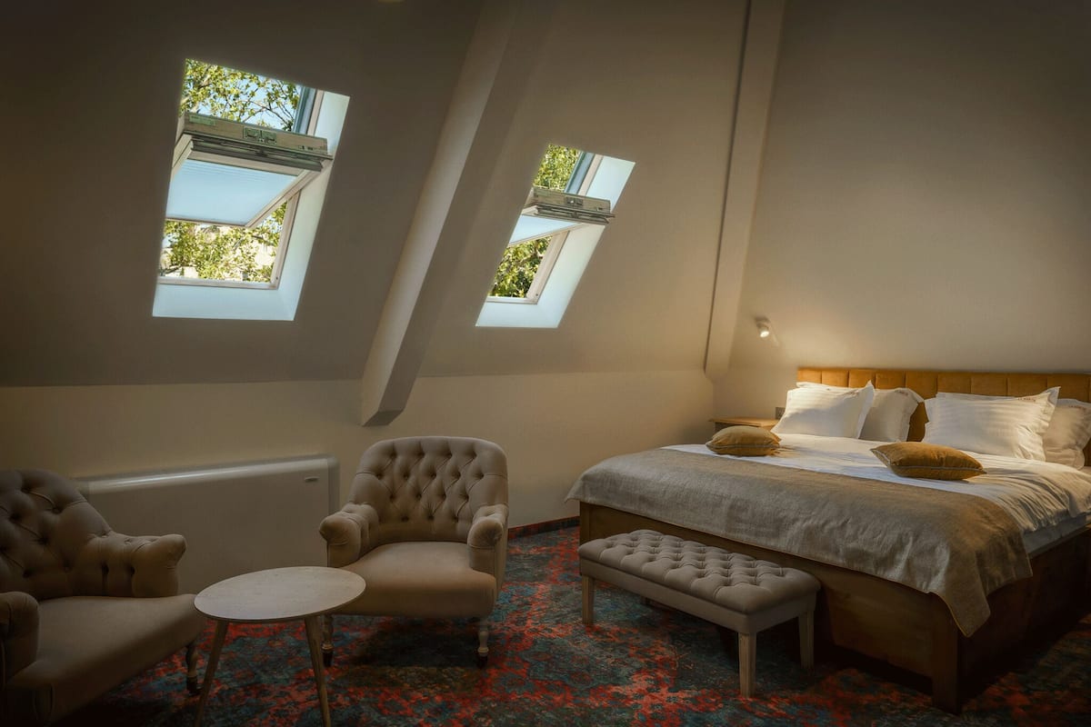 Une chambre à coucher comprenant un lit, deux fauteuils, une petite table et deux fenêtres de toit.