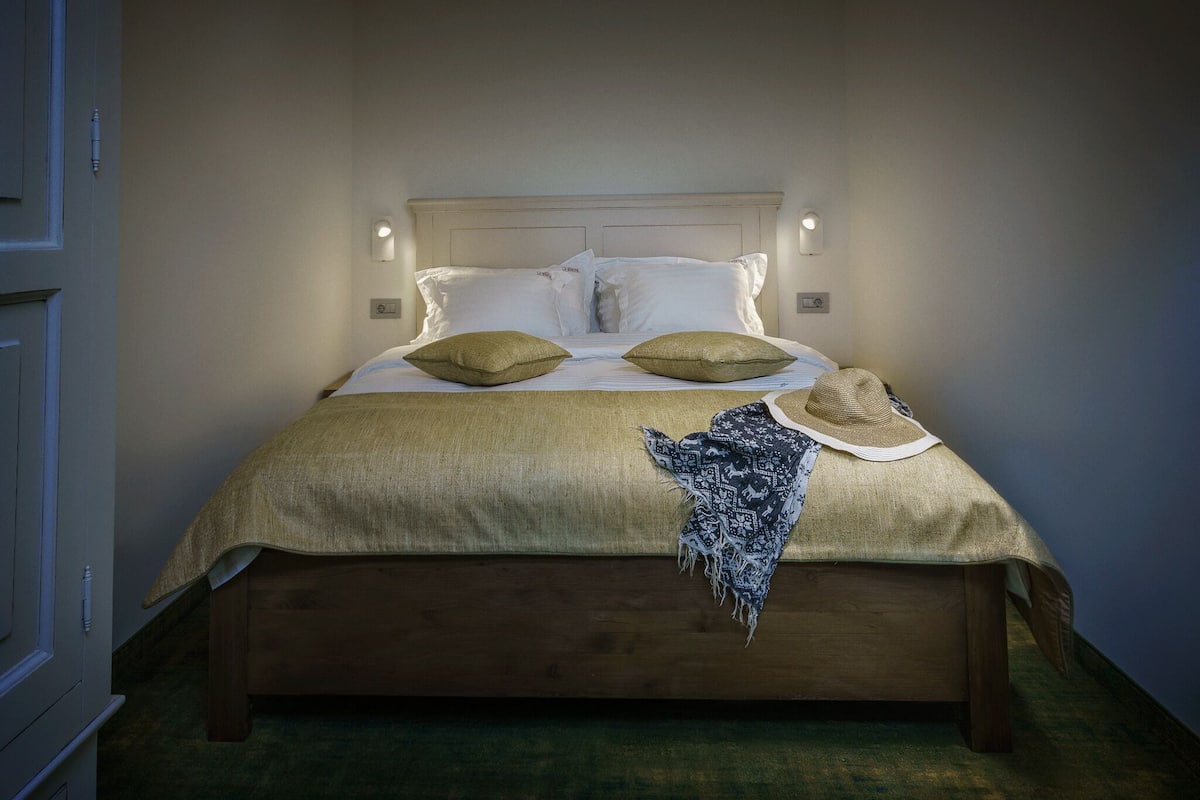 Un lit bien fait, recouvert d’une couvre-lit beige, avec deux oreillers et un chapeau décoratif posé sur le lit.