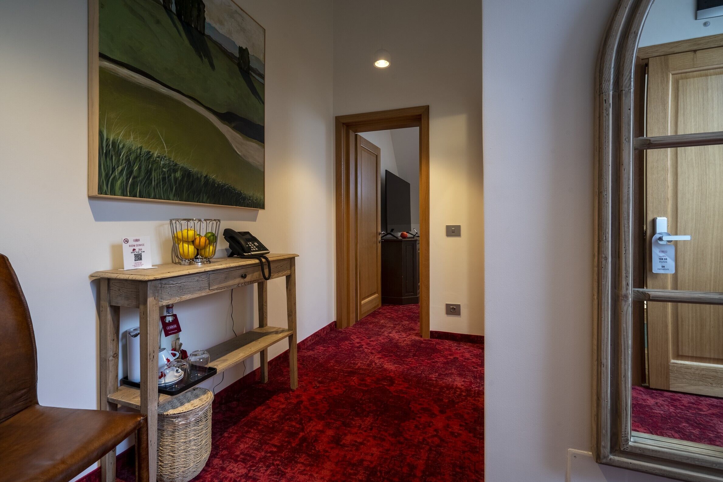 Un pasillo con alfombra roja, una consola de madera con un teléfono y una cesta, y un cuadro en la pared.