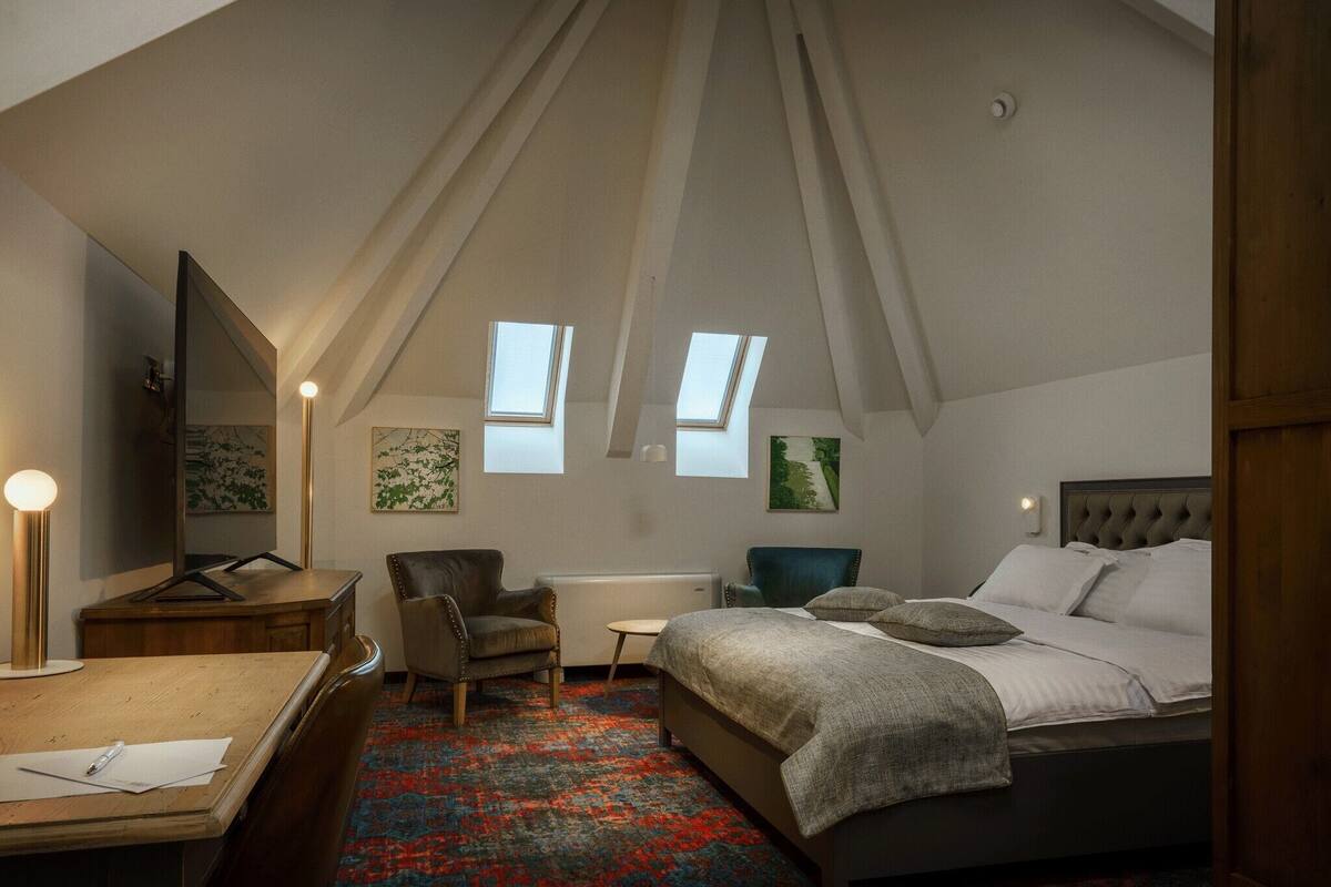 Une chambre à coucher comprenant un lit, un bureau, une chaise, un radiateur et deux fenêtres.