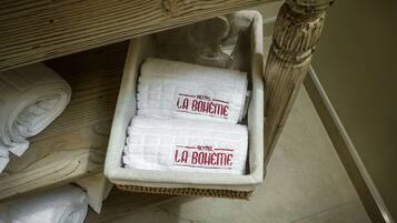 Un panier en osier contenant des serviettes pliées, sur lesquelles est imprimé le nom « HÔTEL LA BOWME », est placé sous une structure en bois.