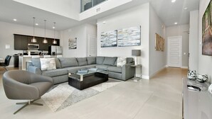 Un salon moderne avec un canapé d’angle, une table basse en verre et un fauteuil gris.