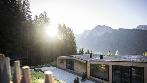 A modern house with large windows, a stone pathway, and a view of mountains.