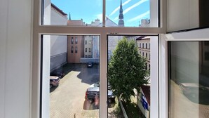 Blick durch ein Fenster auf einen Innenhof mit einem Baum, parkenden Autos und Gebäuden, darunter ein Kirchturm.