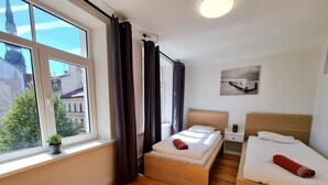 Ein Hotelzimmer mit zwei Betten, einem Vorhangfenster, einer kleinen Pflanze und Blick auf Gebäude.