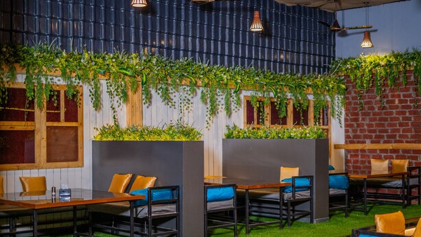 A restaurant with wooden tables and chairs, green plants on the walls, and a brick wall. - hotel mari aai residency (Panvel)
