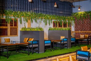 A restaurant with wooden tables and chairs, green plants on the walls, and a brick wall. - hotel mari aai residency (Panvel)