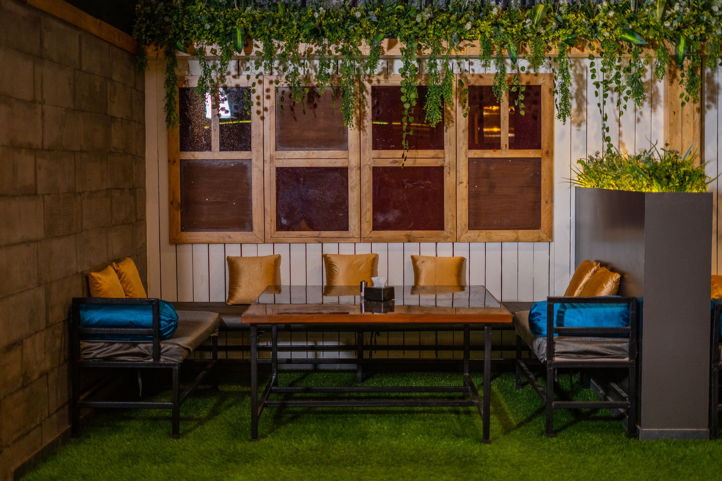 Un rincón acogedor con una mesa y sillas de madera, rodeado de ventanas amplias y plantas verdes.