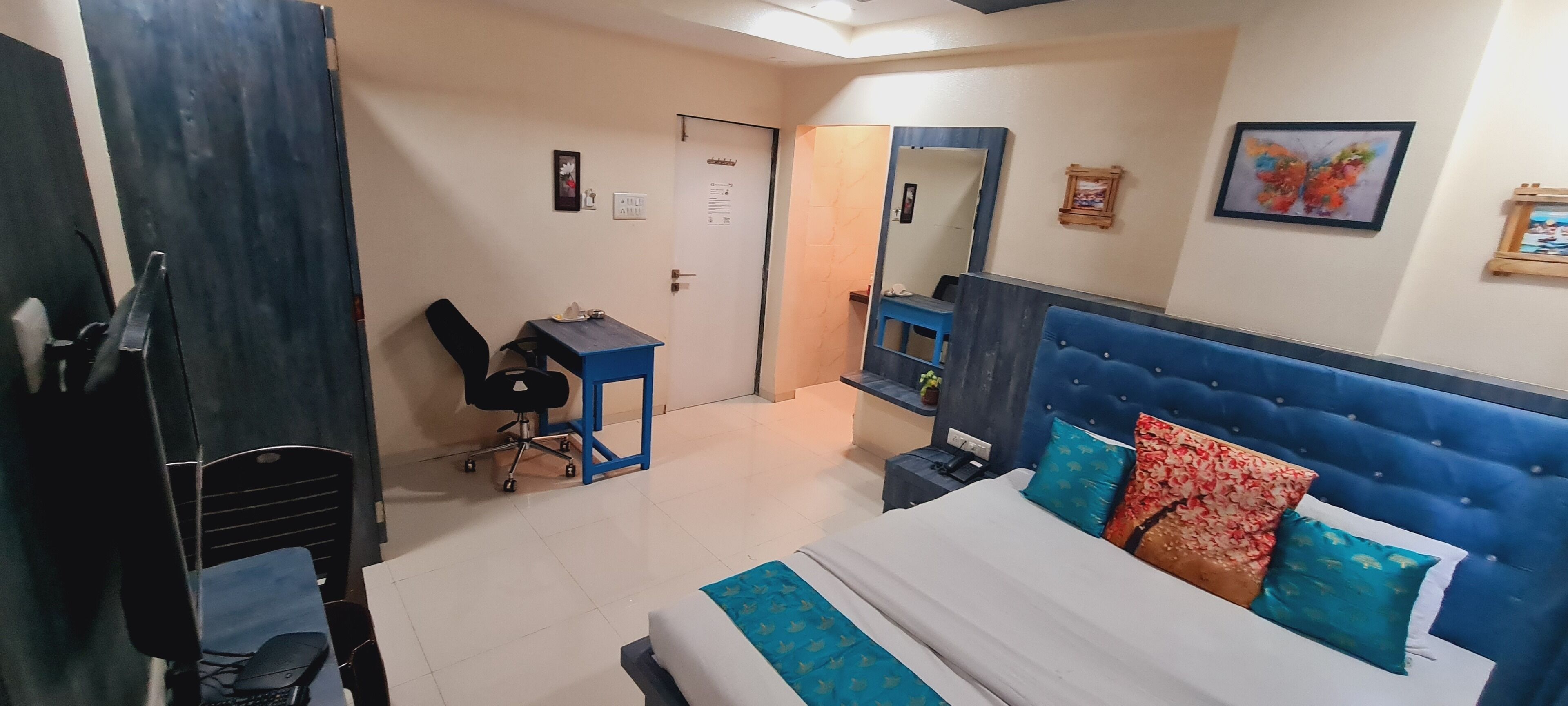 A hotel room with a bed, a desk, a chair, a mirror, and a door.