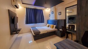 A modern bedroom with a bed, a desk, a chair, a TV, and a ceiling light. - hotel mari aai residency (Panvel)