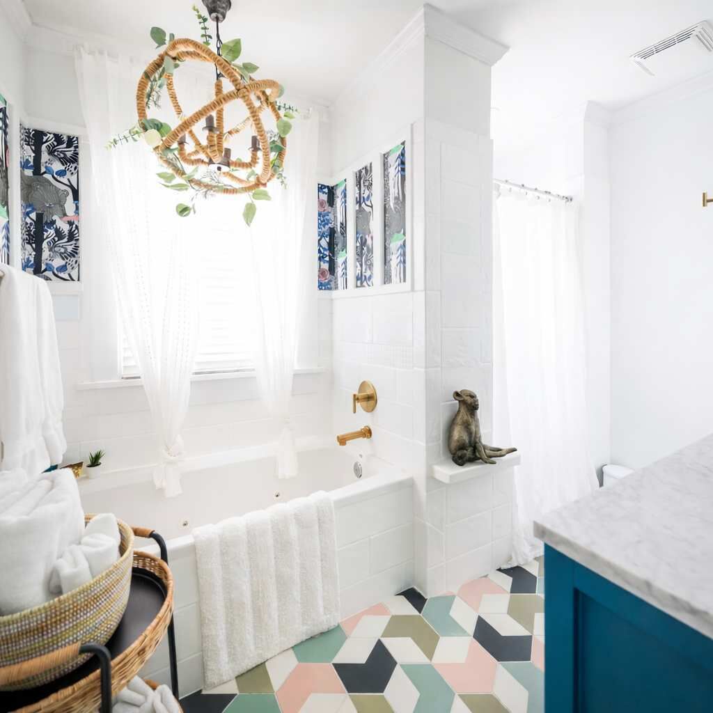 A modern bathroom with a freestanding bathtub, a decorative chandelier, and a colorful geometric floor pattern.
