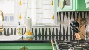 A kitchen with green cabinets, a black countertop, and a window with yellow curtains.