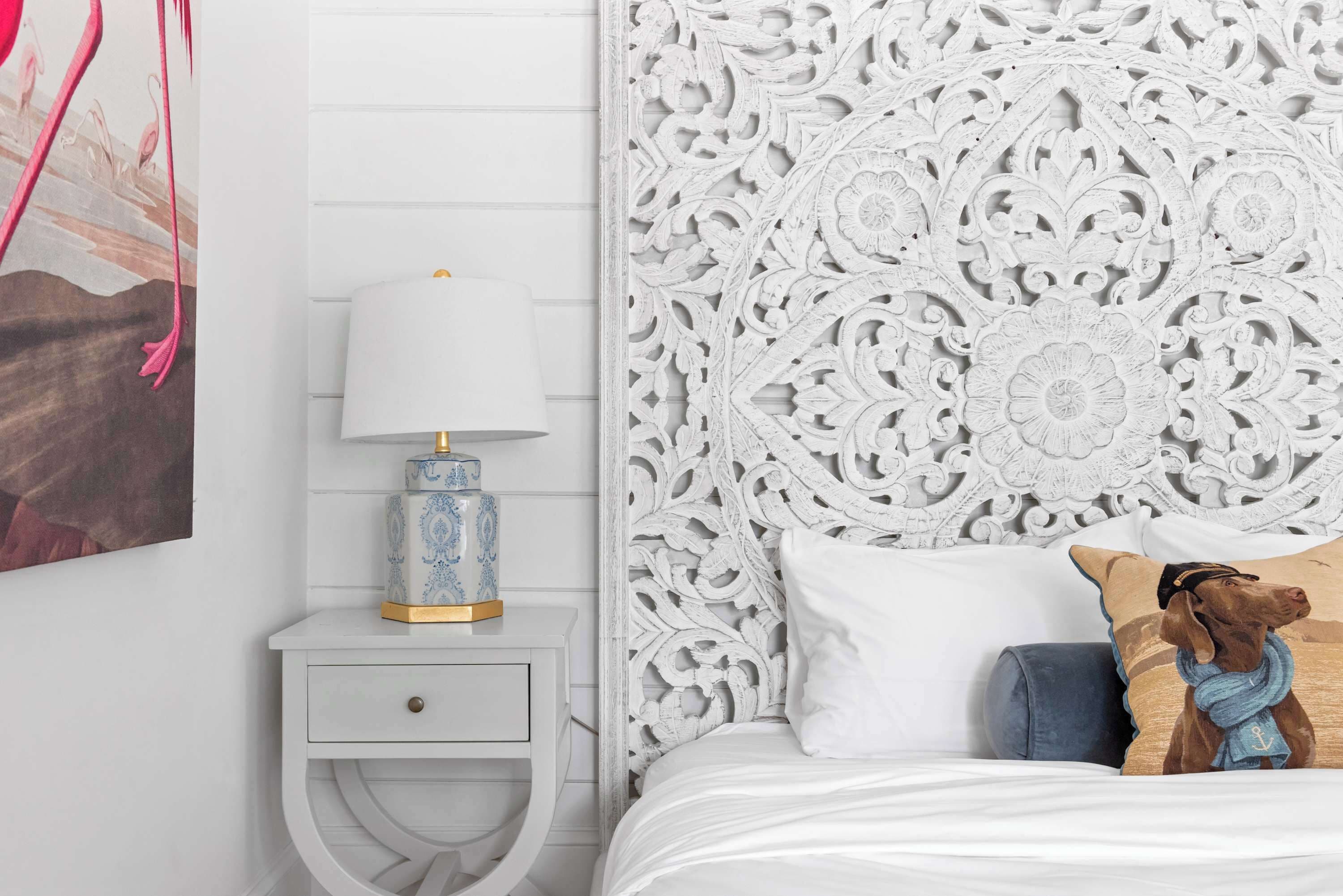 A bedroom with a white headboard, a bedside table with a lamp, and a bed with pillows.