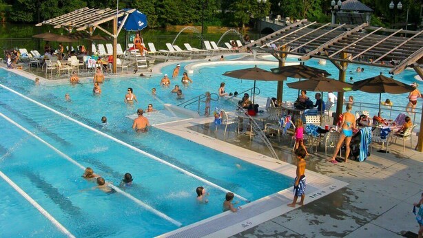 A swimming pool with multiple lanes, sun loungers, umbrellas, and a covered seating area.