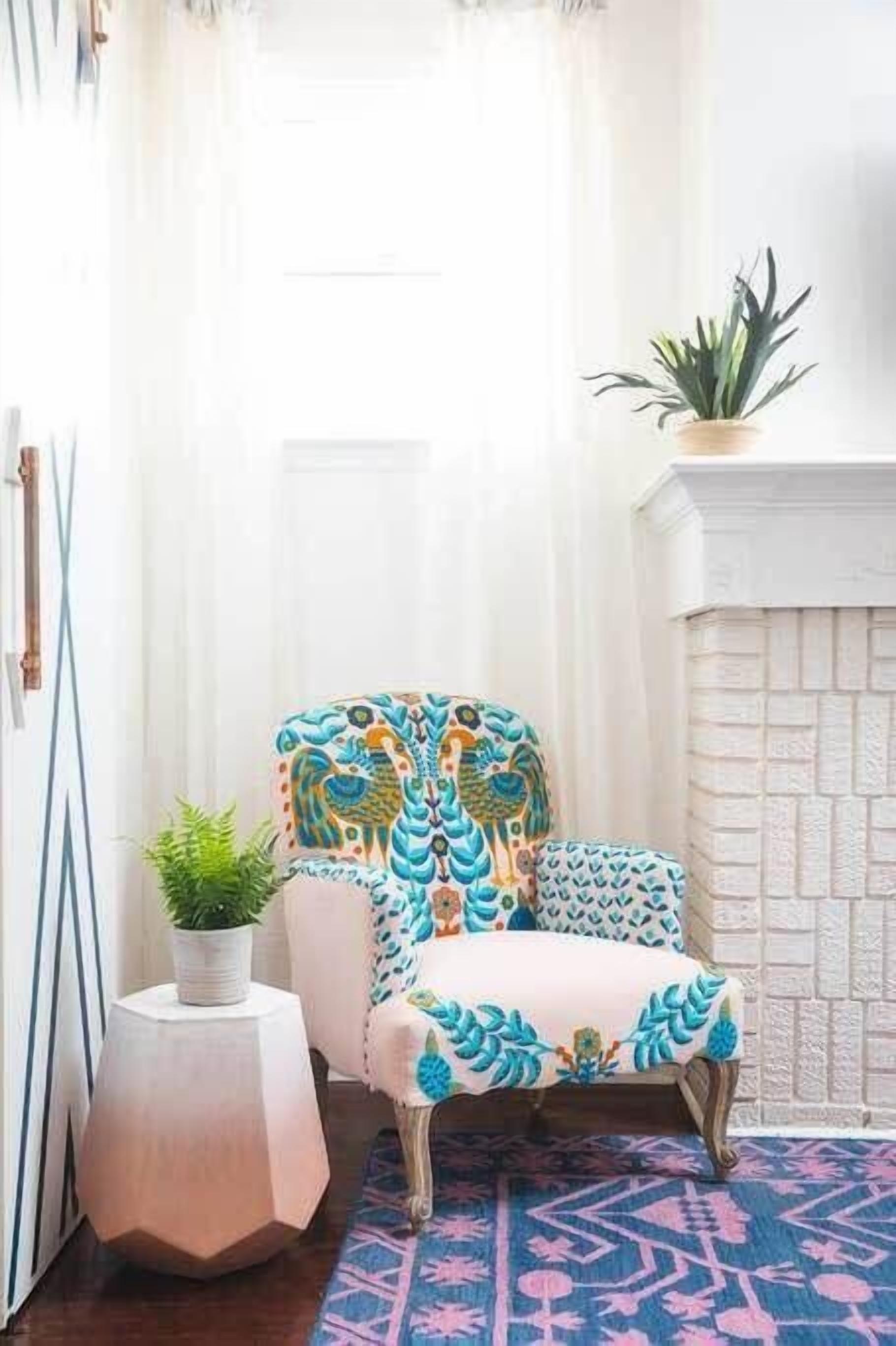 Una habitació amb una poltrona estampada, una llar de pedra blanca i un rug geometric.