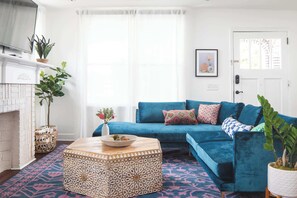 Uma sala de estar com um sofá azul, um banquinho estampado e uma lareira.