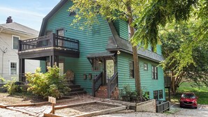 A two-story house with a green exterior, a front porch, and a red car parked in the driveway. - Lucky Leopard (Atlanta)