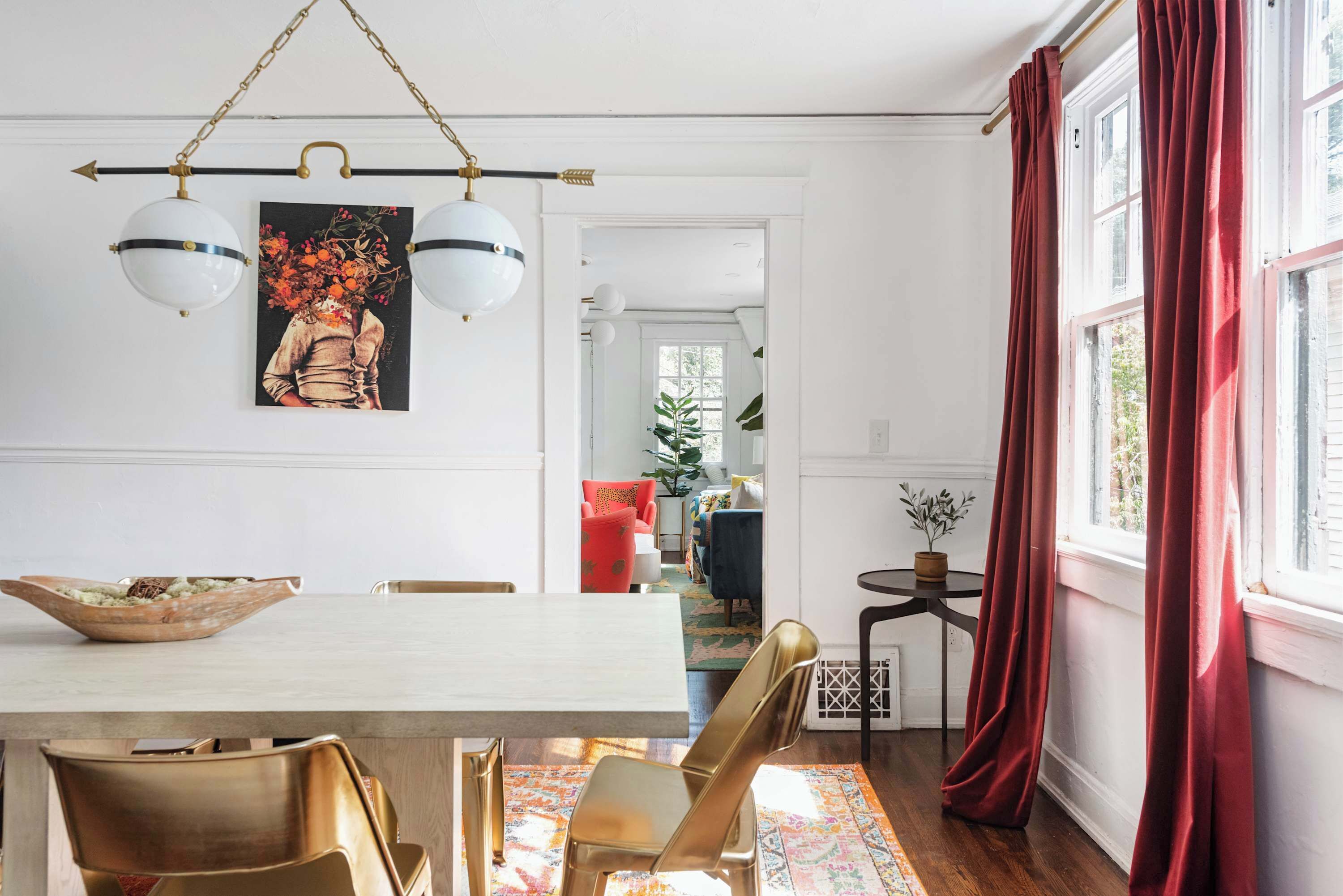 A dining area with a white table, gold chairs, and a hanging light fixture.
