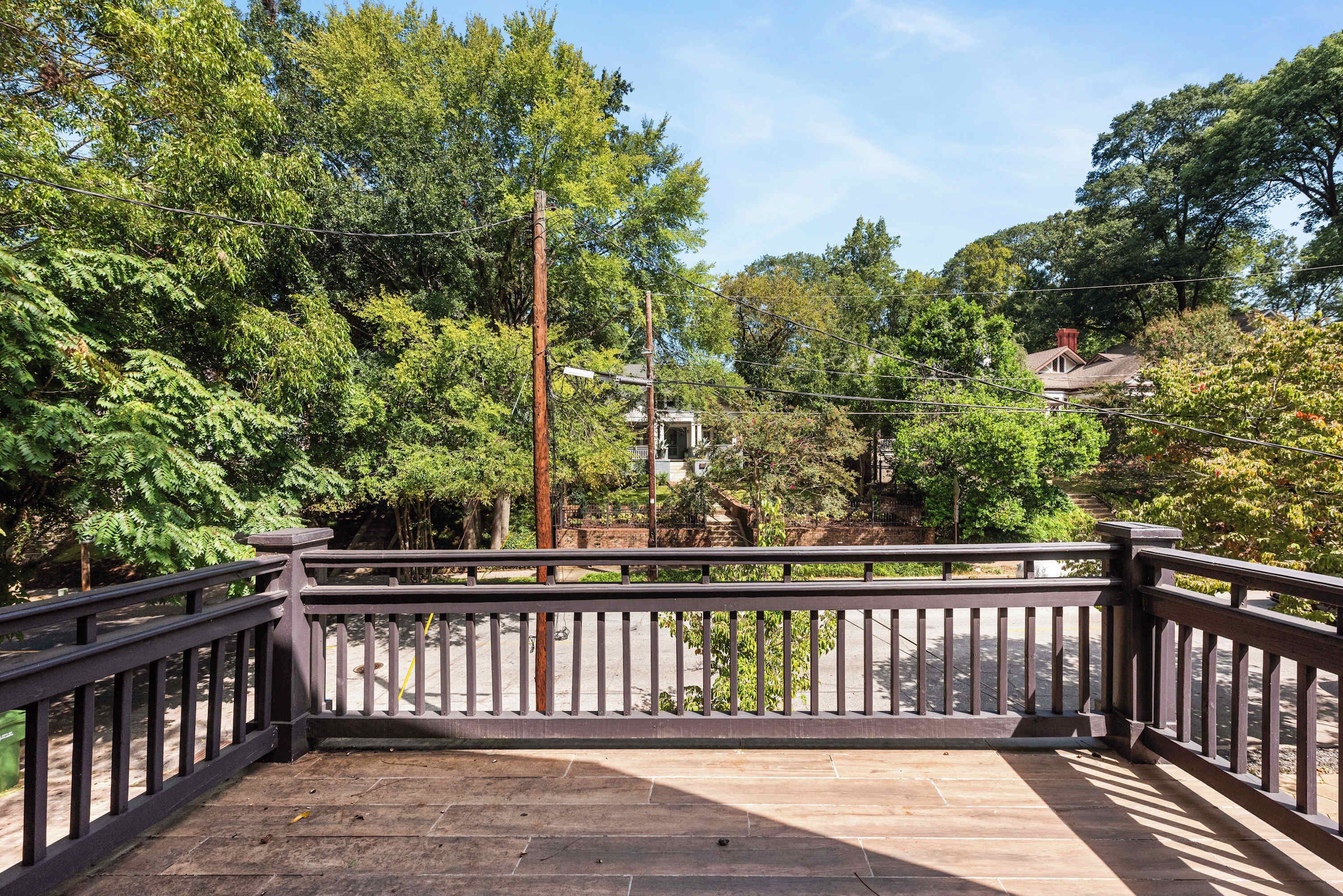 A wooden deck with a metal railing, surrounded by lush green trees and a clear sky.