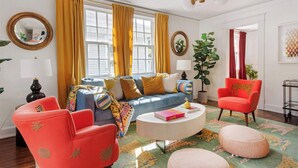 A living room with a blue sofa, red chairs, a round coffee table, and a colorful rug. - Lucky Leopard (Atlanta)