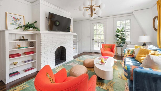 A living room with a white brick fireplace, a flat-screen TV, a colorful rug, and a blue sofa with yellow pillows. - Lucky Leopard (Atlanta)