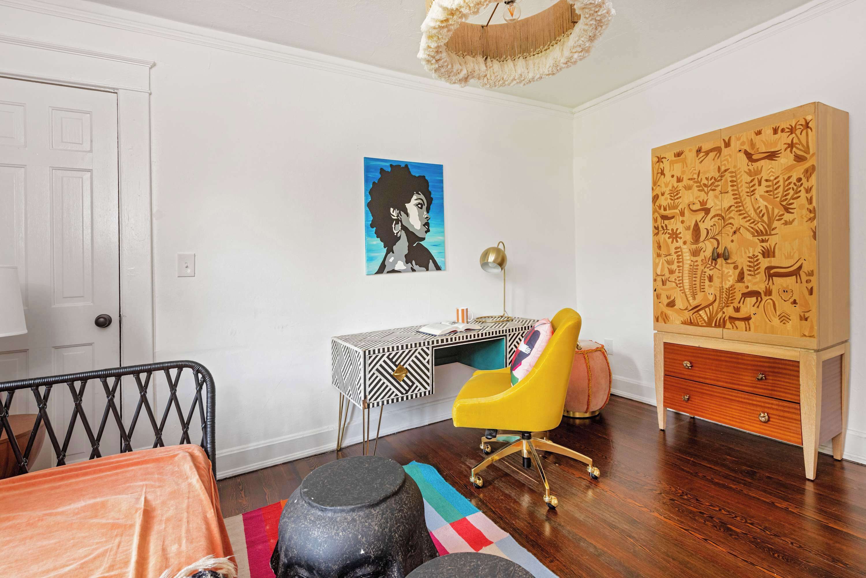 A room with a desk, a yellow chair, a large wooden cabinet, and a colorful rug.