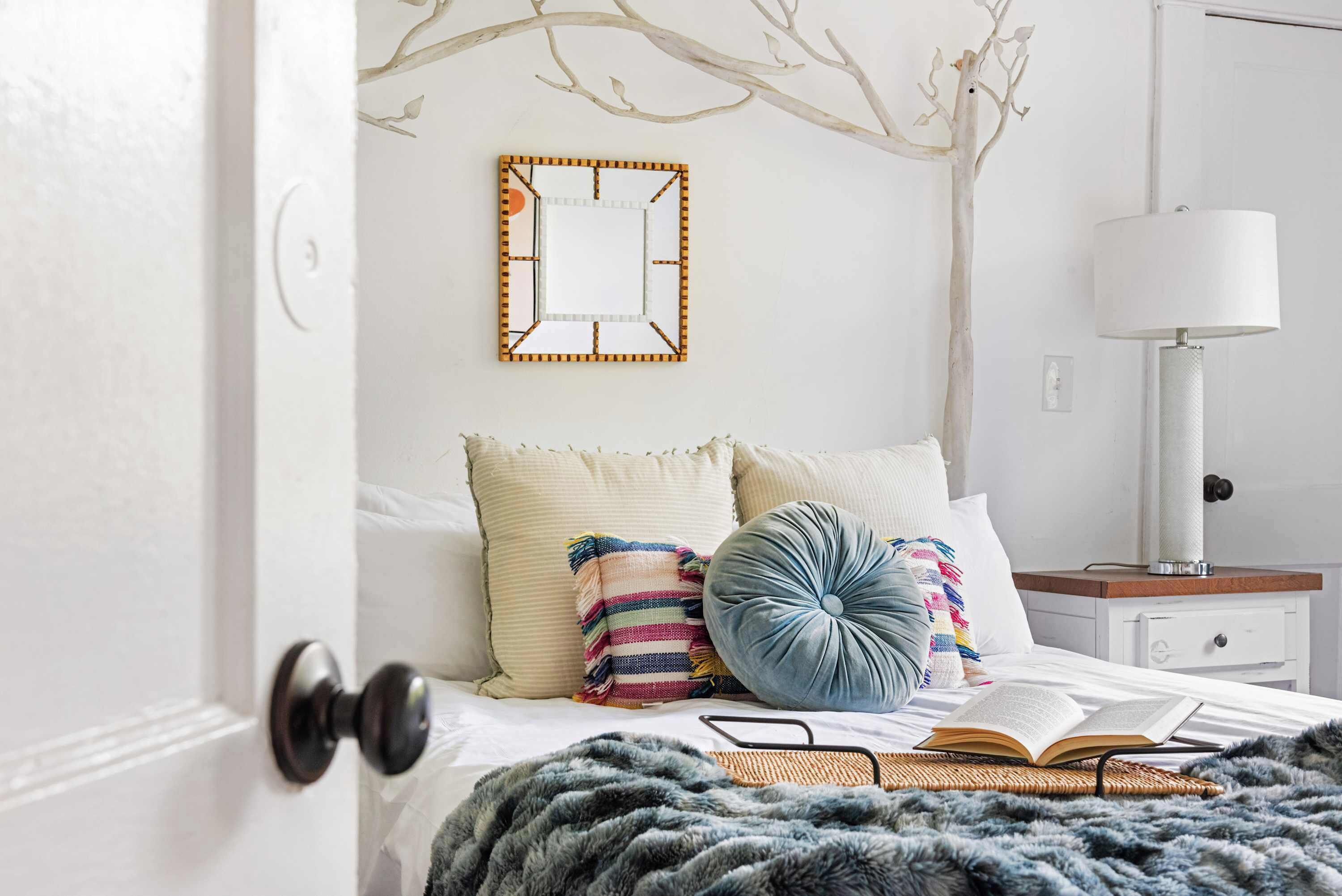 A neatly arranged bedroom with a bed, pillows, a mirror, and a bedside lamp.