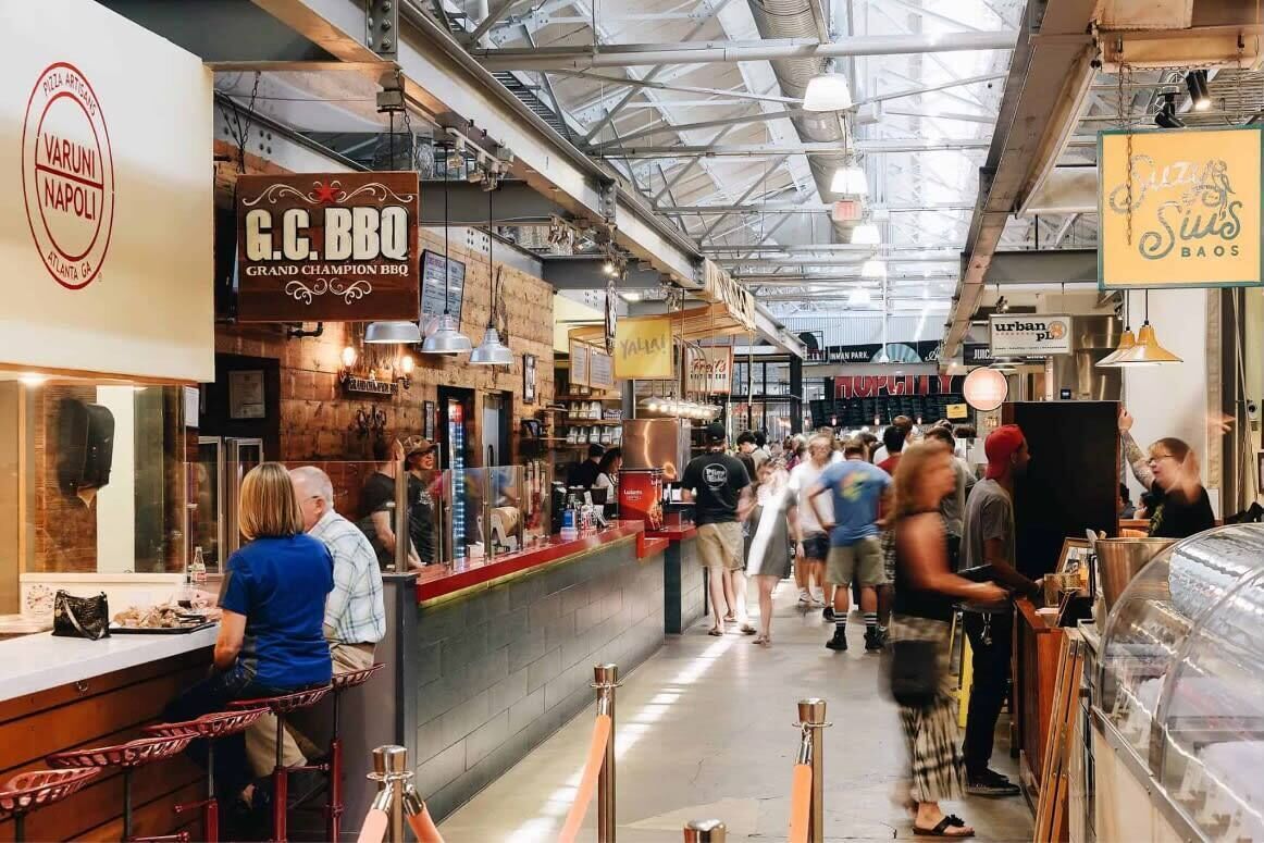 A bustling indoor market with various food stalls, including a barbecue restaurant and a furniture store.