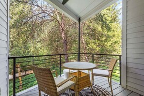 A balcony with wicker furniture, a small table, and a view of trees.