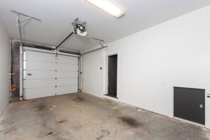 A garage with a closed garage door, a ceiling-mounted light fixture, and a door leading to another room.