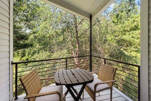A balcony with a table and two wicker chairs, overlooking a forested area.