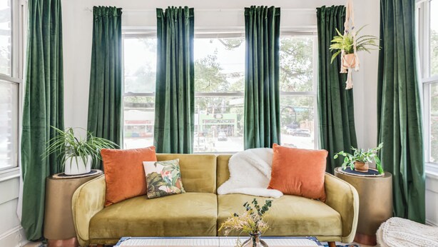 A room with a sofa, two side tables with potted plants, a vase with flowers, and a patterned rug. - Morehaus (Atlanta)