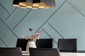 Un interior moderno con un diseño geométrico en la pared, un jarrón central con flores secas y sillas tapizadas en negro.