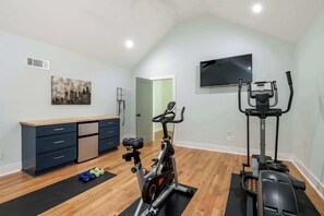 Uma academia em casa com uma bicicleta ergométrica, elíptico e pesos em um piso de madeira.