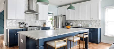 A modern kitchen with white cabinets, a central island with bar stools, and pendant lighting.