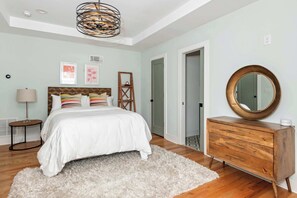 A bedroom with a bed, a wooden dresser, a mirror, and a fluffy rug.