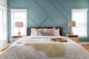 A bedroom with a bed, two bedside tables with lamps, a window with blinds, and a decorative wall panel.