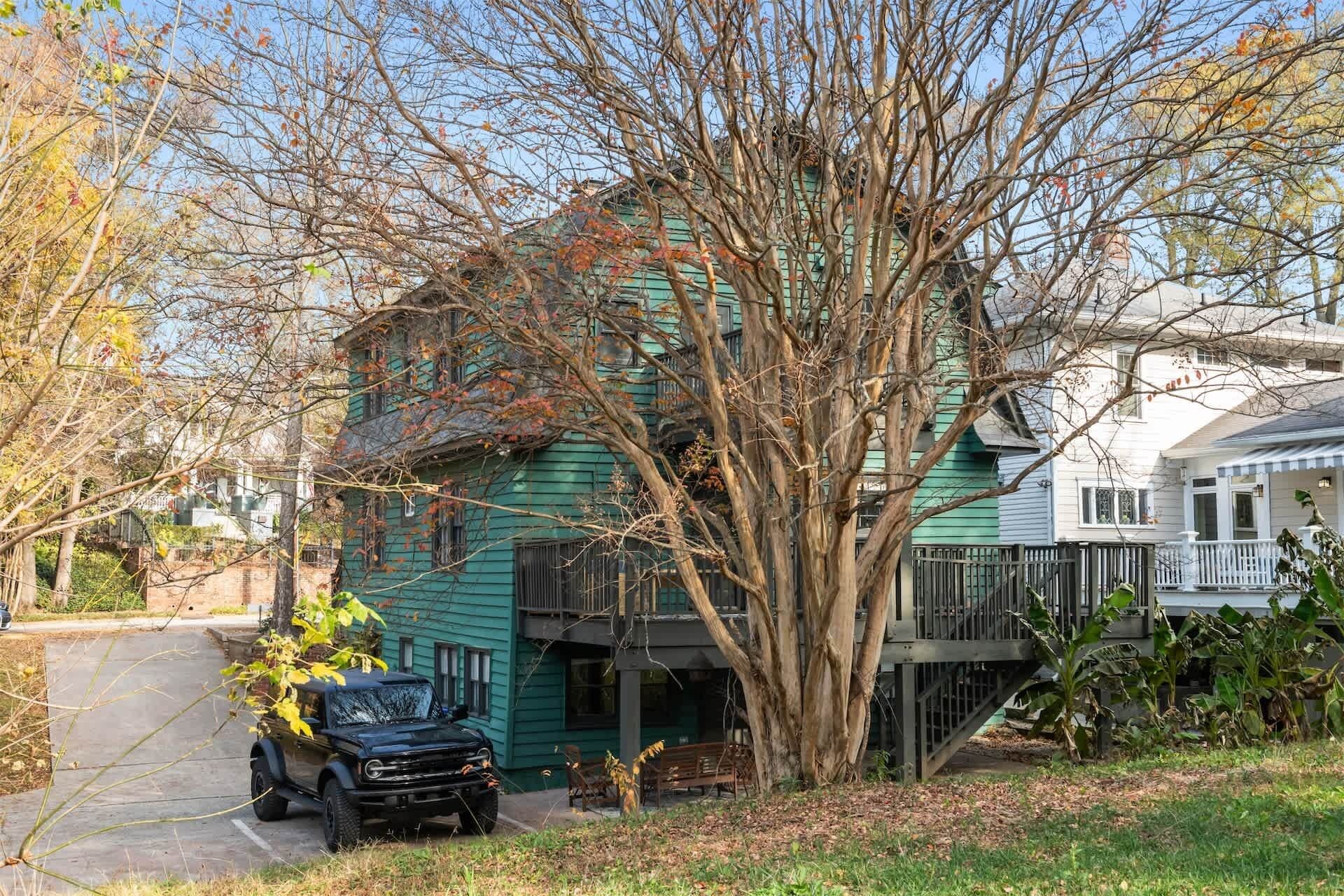 A two-story house with a green exterior, a tree in front, and a parked vehicle.