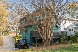 A two-story house with a green exterior, a tree in front, and a parked vehicle.