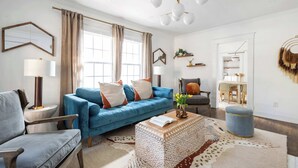 A modern living room with a blue sofa, a patterned ottoman, and a chandelier. - Golden Gazelle (Atlanta)