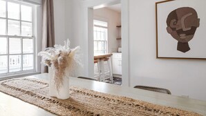 A dining area with a large window, a woven rug, a vase with dried plants, and a framed artwork on the wall. - Golden Gazelle (Atlanta)