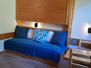Un lit en bois avec une couvre-lit bleue et des oreillers, une tête de lit en bois et une petite chaise en bois.