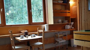 A cozy cabin with a wooden interior, a dining table with chairs, a kitchen area with shelves, and a window with a view of trees. - Studio in Center for 2, Free Wifi (Les Arcs 1800)